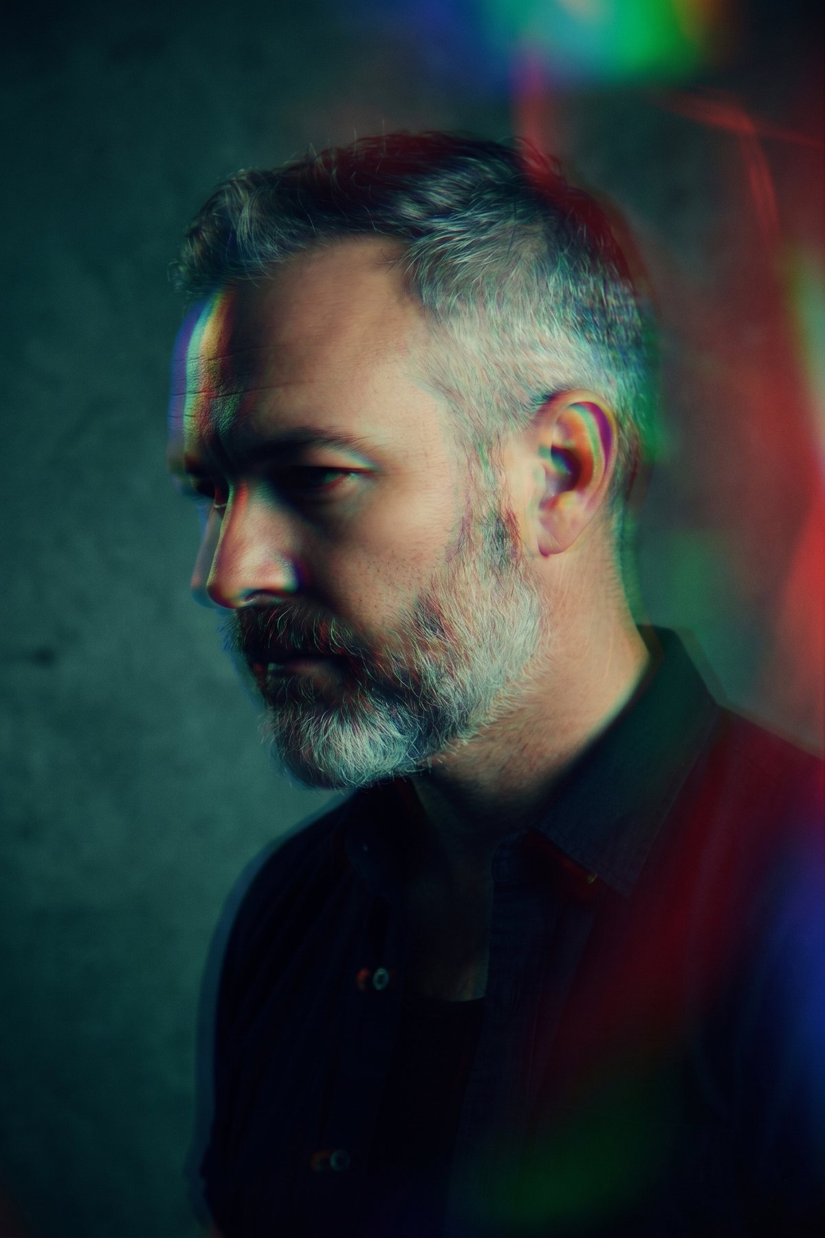 Chris Franzen in profile against a teal concrete wall, light splitting into color across his face.